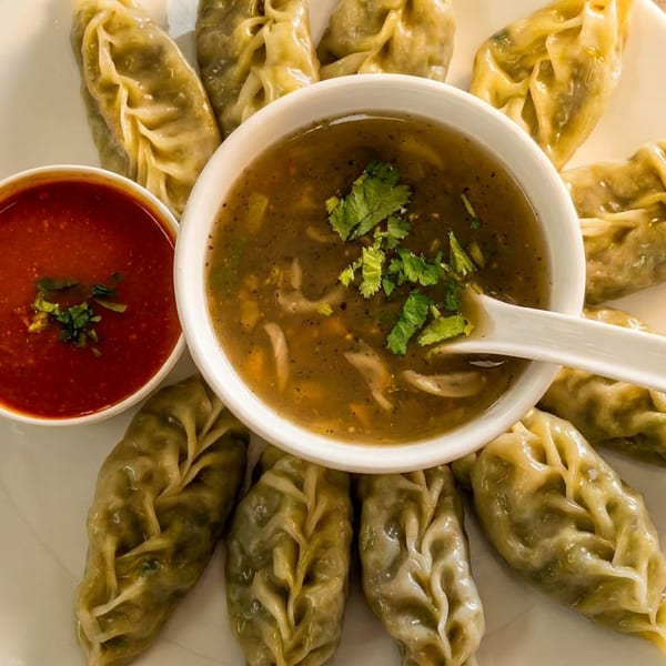 Steamed momos arranged on a white plate with two dipping sauces, one red and one brown.