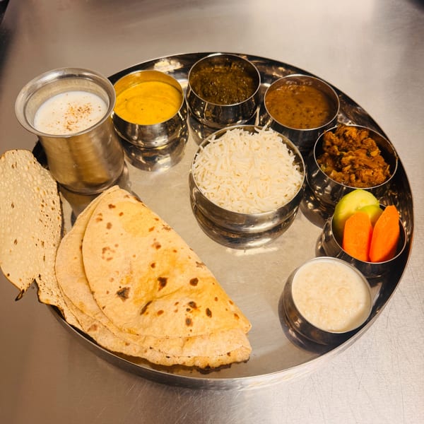 Full thali platter with dal, curries, rice, roti, papad, and dessert