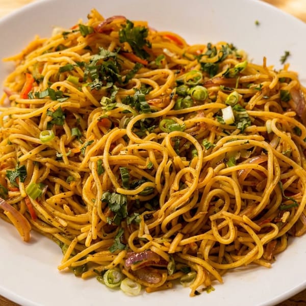 A white plate filled with stir-fried noodles, garnished with fresh green herbs and scallions.