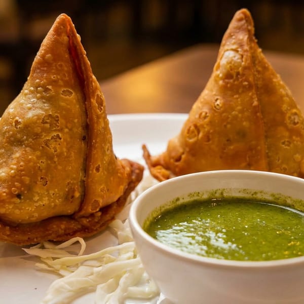 Two golden-brown samosas with a side of green chutney on a white plate.